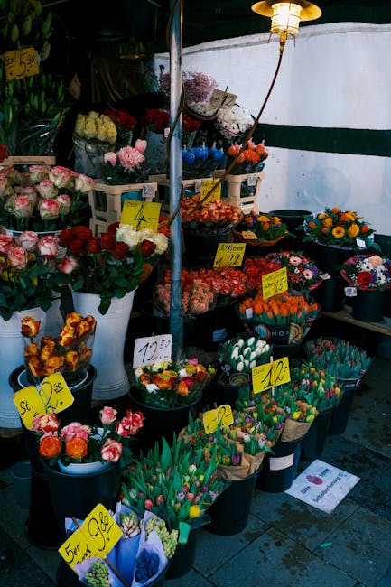 An outdoor flower stall displaying an assortment of fresh floral arrangements and bouquets. The arrangement includes vibrant pink, red, orange, yellow, and white flowers, with some featuring mixed col